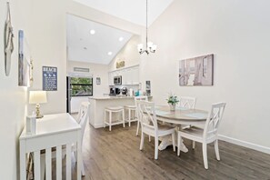 A modern kitchen with white cabinetry, a central island, and a dining area with white chairs and a round table.