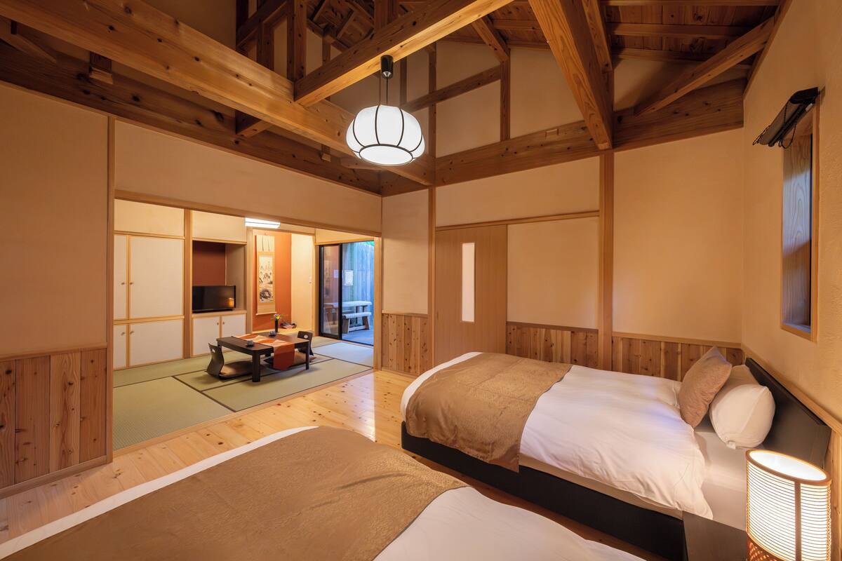 A traditional Japanese-style room with tatami flooring, wooden beams, and a bed with a headboard.