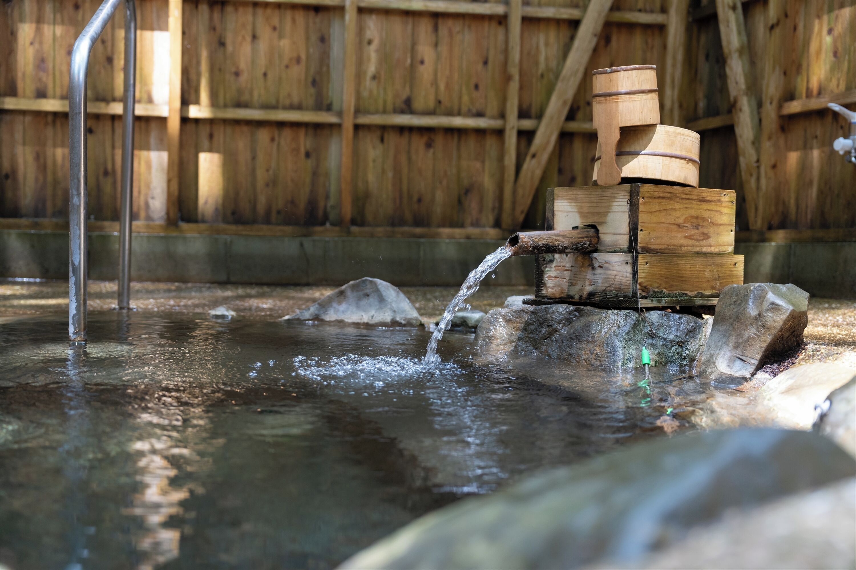 Eine Holzkonstruktion mit einem Wasserspiel, darunter eine Holzbütte und ein Metall-Ausguss.