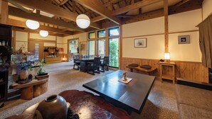 A spacious room with a high ceiling, wooden beams, a large dining table, and a cozy seating area with a leather couch. - Tsuwabuki-no-Hana (Higashisonogi)