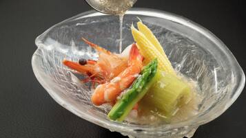 A clear glass bowl containing shrimp, corn, and asparagus on a dark surface.