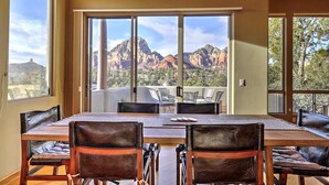 A dining area with a large table and chairs, a view of red rock formations, and a balcony with outdoor seating.