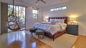 A bedroom with a bed, bedside table, hanging chair, and two ottomans.