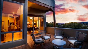 A balcony with wicker chairs and a table, overlooking a scenic landscape during sunset.