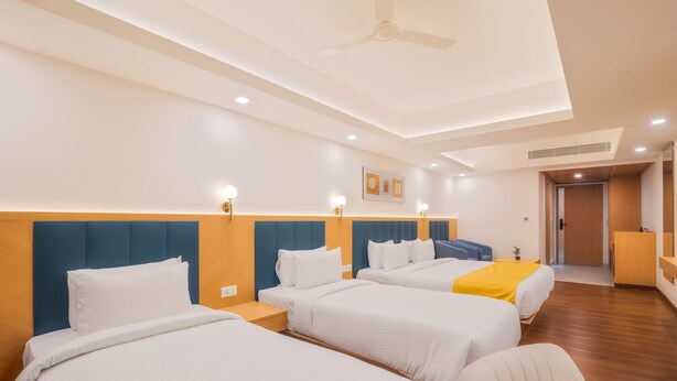 A hotel room with three beds, a ceiling fan, recessed lighting, and a wooden floor. - Hotel Turmeric (Erode)