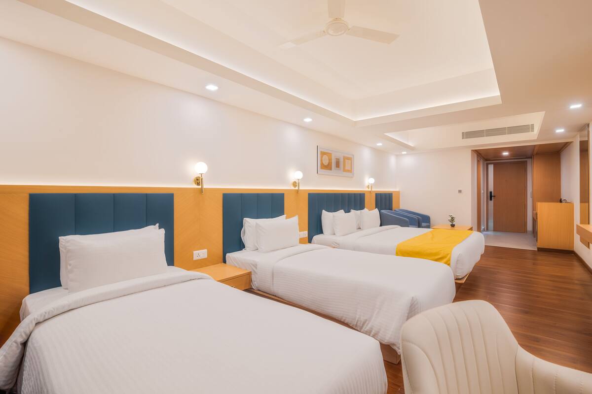 Habitación de hotel con tres camas, ventilador de techo, iluminación empotrada y suelo de madera.