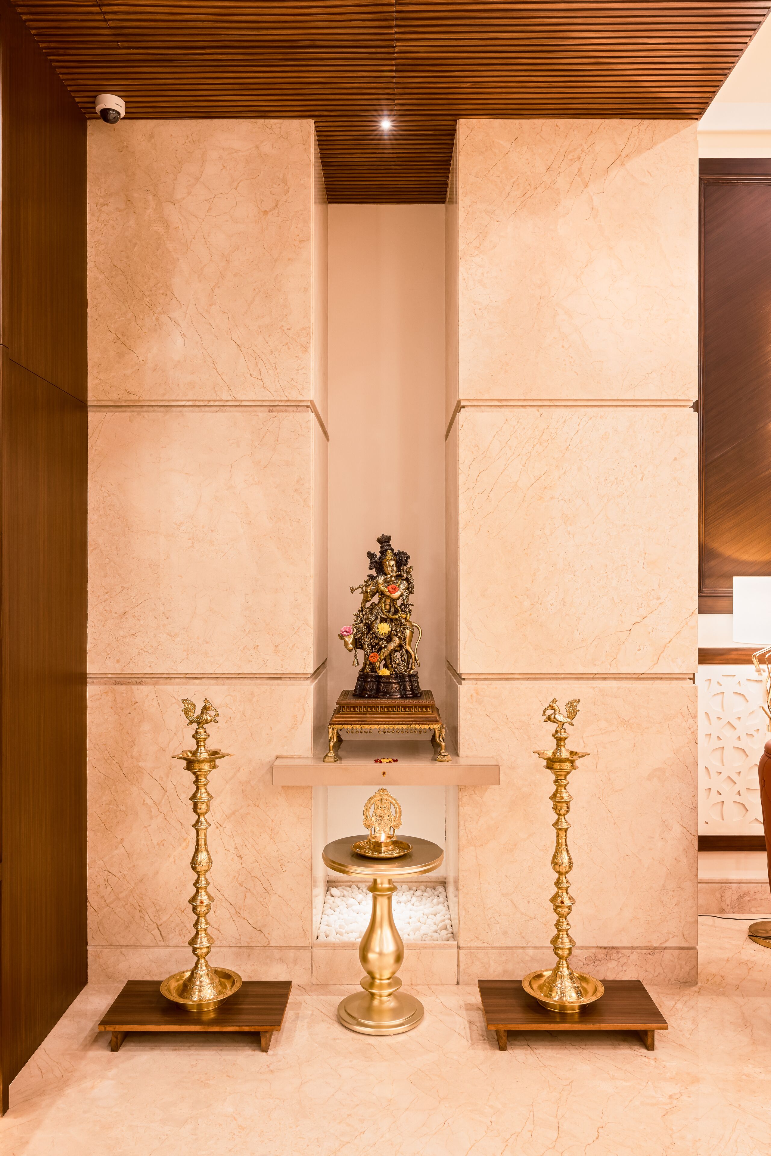 A room with marble walls and a wooden ceiling, featuring a central decorative piece and two golden candelabras on pedestals.