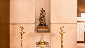 A room with marble walls and a wooden ceiling, featuring a central decorative piece and two golden candelabras on pedestals.