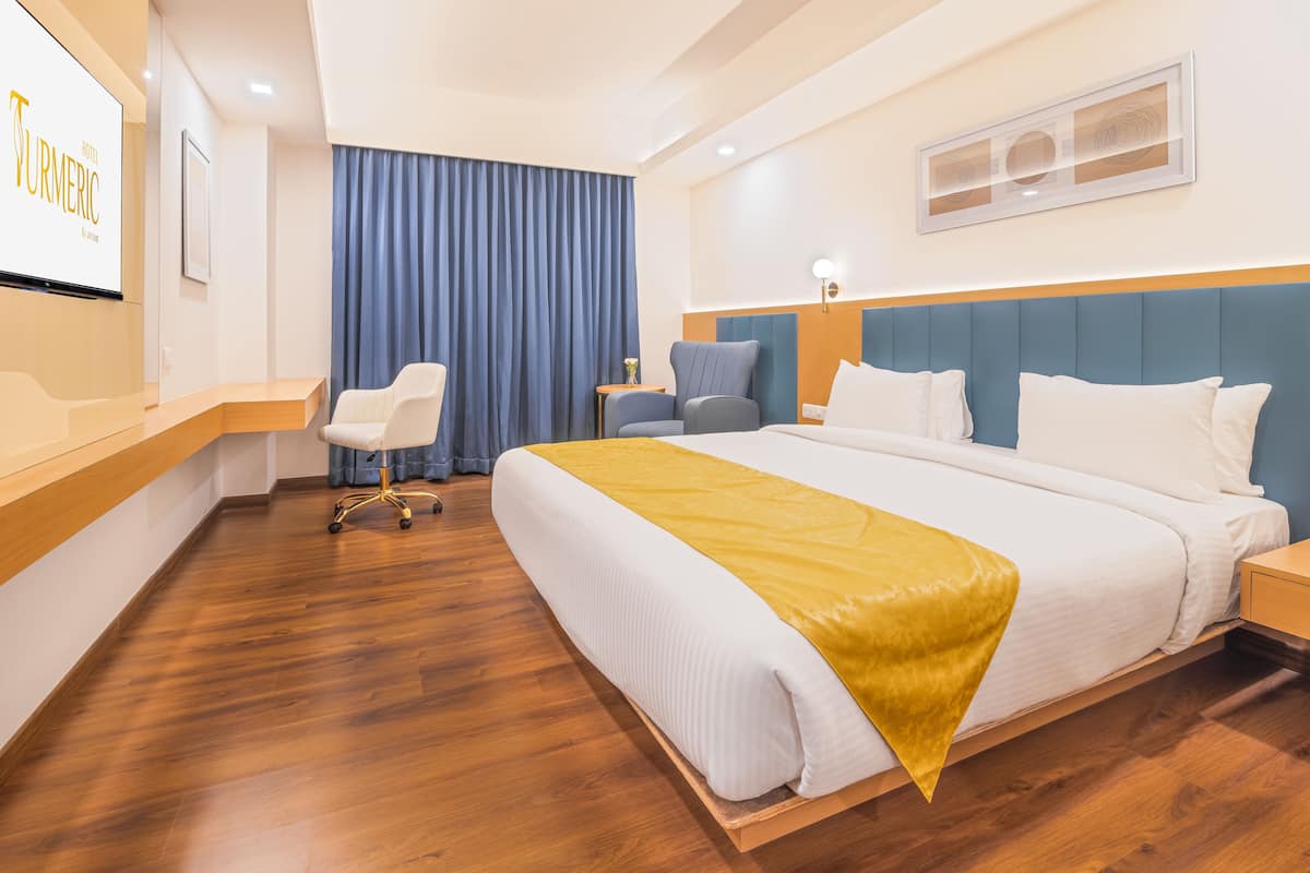 Habitación de hotel con una cama grande, un escritorio con silla, una mesita pequeña y una cortina azul.