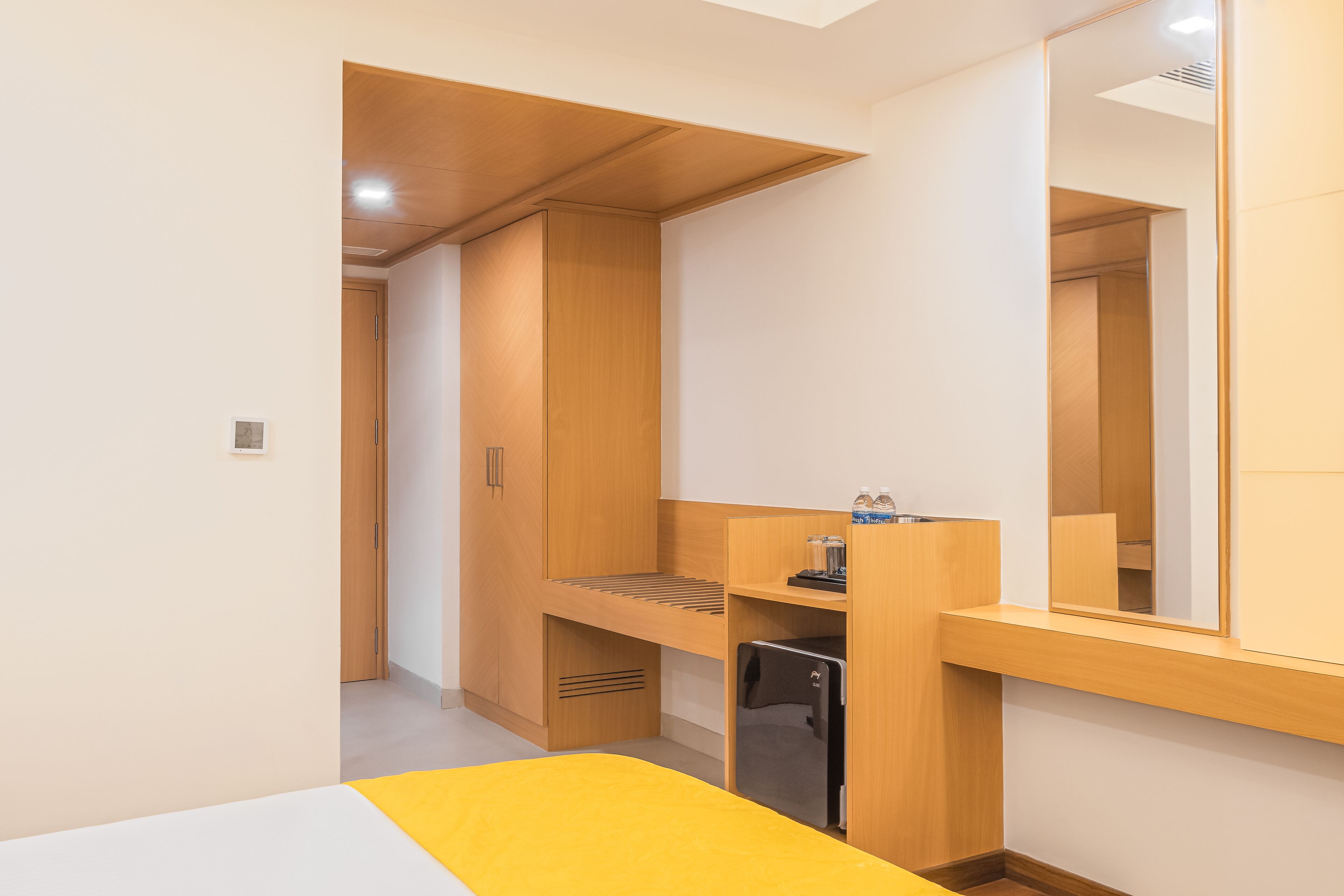 A compact room with a bed, a small desk, a mirror, and built-in wooden storage.