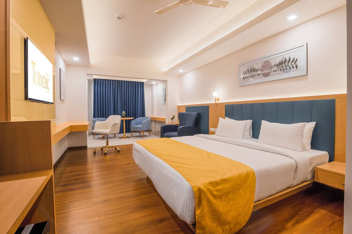 Una habitación de hotel con una cama grande, un escritorio, una silla, una mesita y una cortina azul.