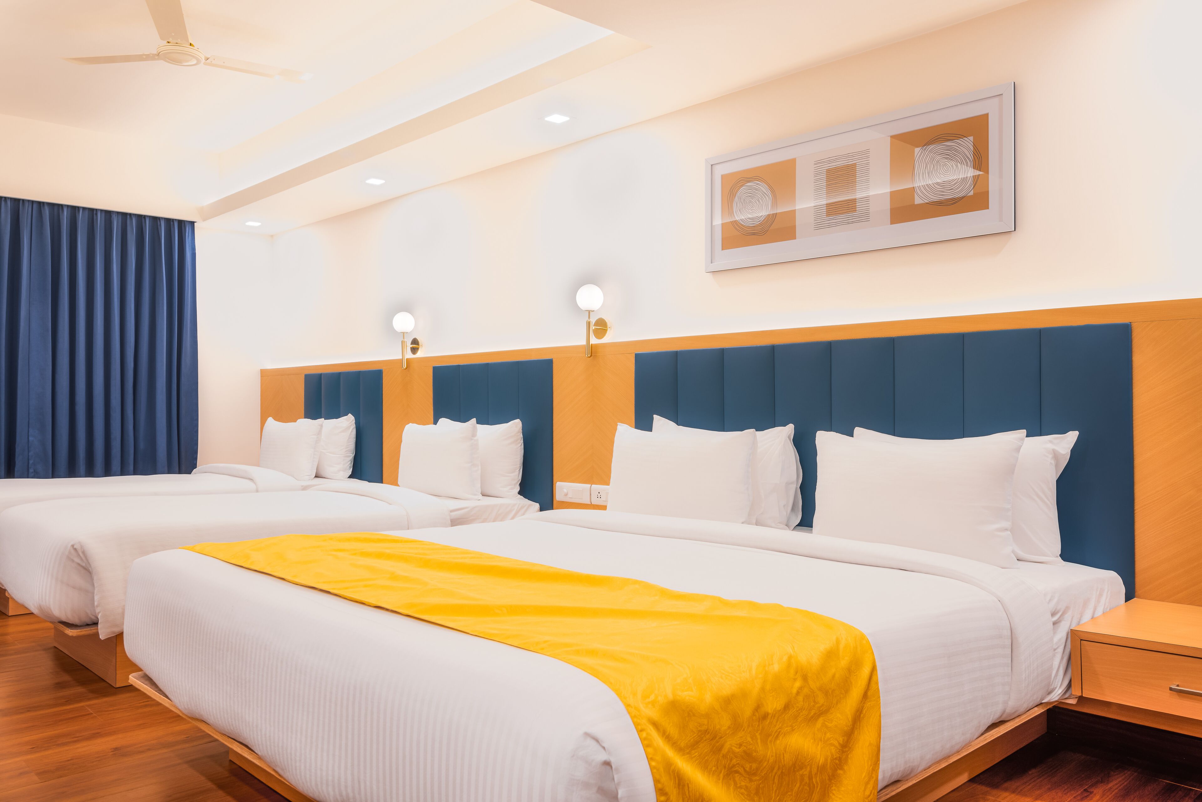 A hotel room with two beds, a ceiling fan, recessed lighting, and a framed artwork on the wall.