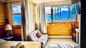 A hotel room with a bed, a sofa, a desk, and a chair. There are curtains on the windows, and a view of the outside. - Cozy Vacation Rental in San Cristóbal de las Casas (San Cristóbal de las Casas)