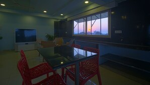 A conference room with a glass table, red chairs, a large TV, and a window with a city view. - Hotel NS Royal Emirates (Hyderabad)