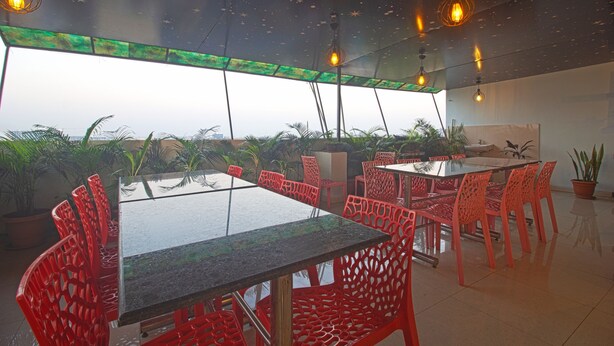 A modern dining area with glass tables and red chairs, featuring a starry ceiling design and potted plants. - Hotel NS Royal Emirates (Hyderabad)