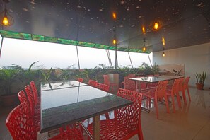 Un espace repas moderne avec des tables en verre et des chaises rouges, agrémenté d’un plafond décoré de motifs étoilés et de plantes en pot.