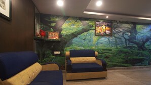 A room with two blue armchairs and a sofa, a mural of a forest, and a framed picture on the wall. - Hotel NS Royal Emirates (Hyderabad)