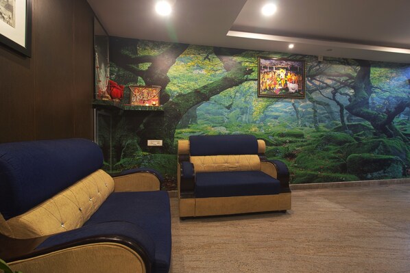 A room with two blue armchairs and a sofa, a mural of a forest, and a framed picture on the wall.