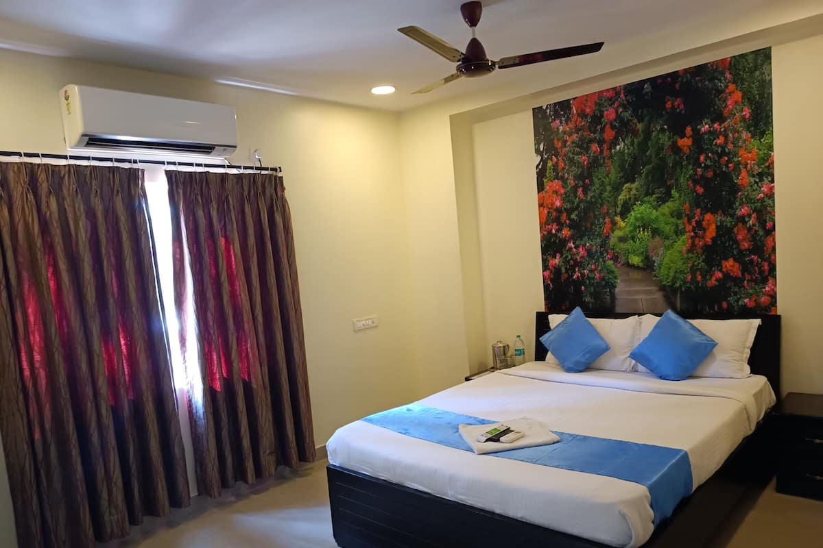 Ein Hotelzimmer mit Bett, Vorhängen, einer Klimaanlage, einem Deckenventilator und einem Wandbild mit floralem Muster.