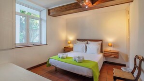 A bedroom with a bed, two bedside tables, a chair, a window, and a wooden ceiling beam.