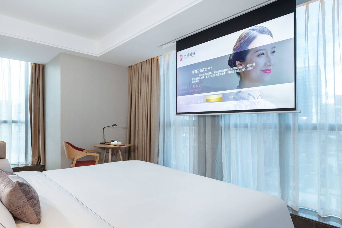 A hotel room with a bed, a desk with a lamp, and a TV screen displaying a welcome message.