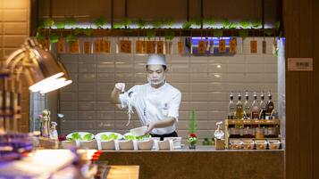 A chef preparing noodles at a counter with a tiled backsplash and shelves of condiments.