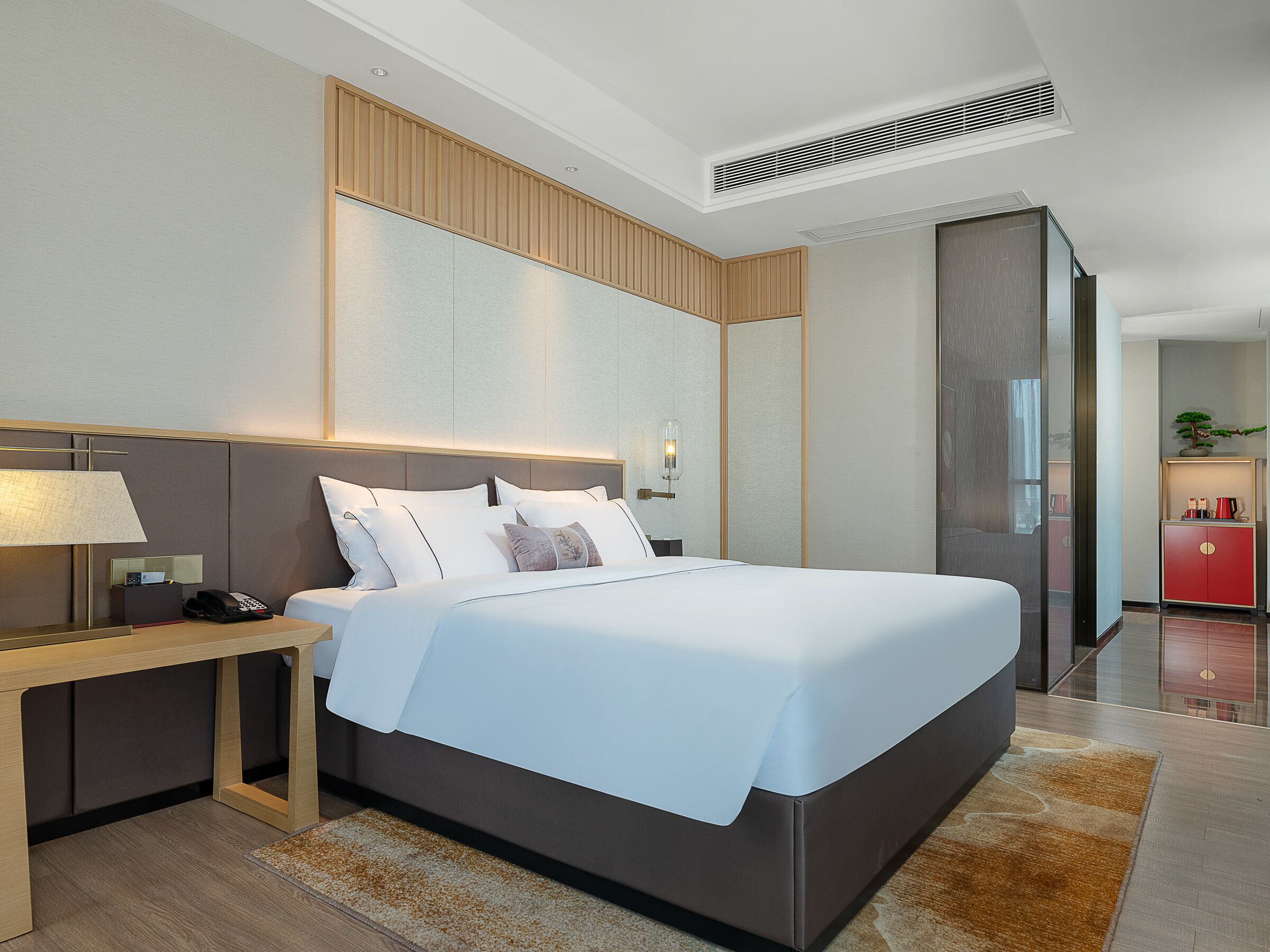 A modern hotel room with a large bed, bedside table, lamp, and a red cabinet.