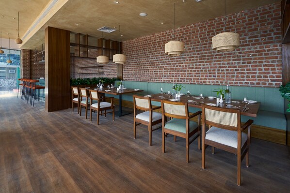 Un restaurante con mesas y sillas de madera, paredes de ladrillo y lámparas colgantes.