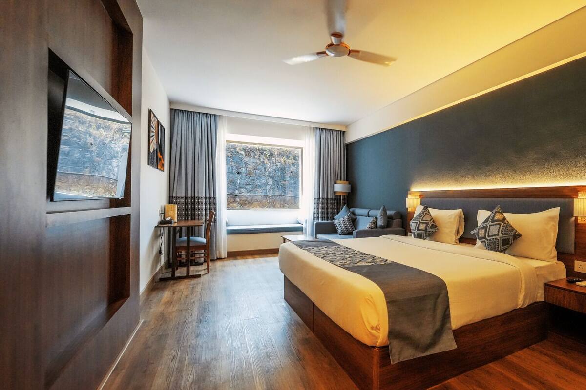 A modern hotel room with a large bed, a desk, and a view of the outdoors.