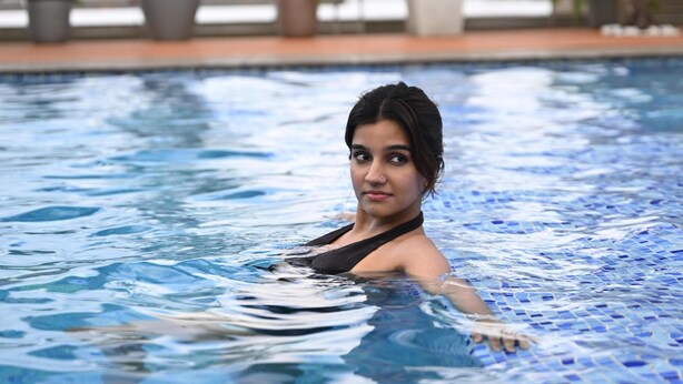 Una persona en una piscina con suelo de baldosas y plantas en macetas al fondo.