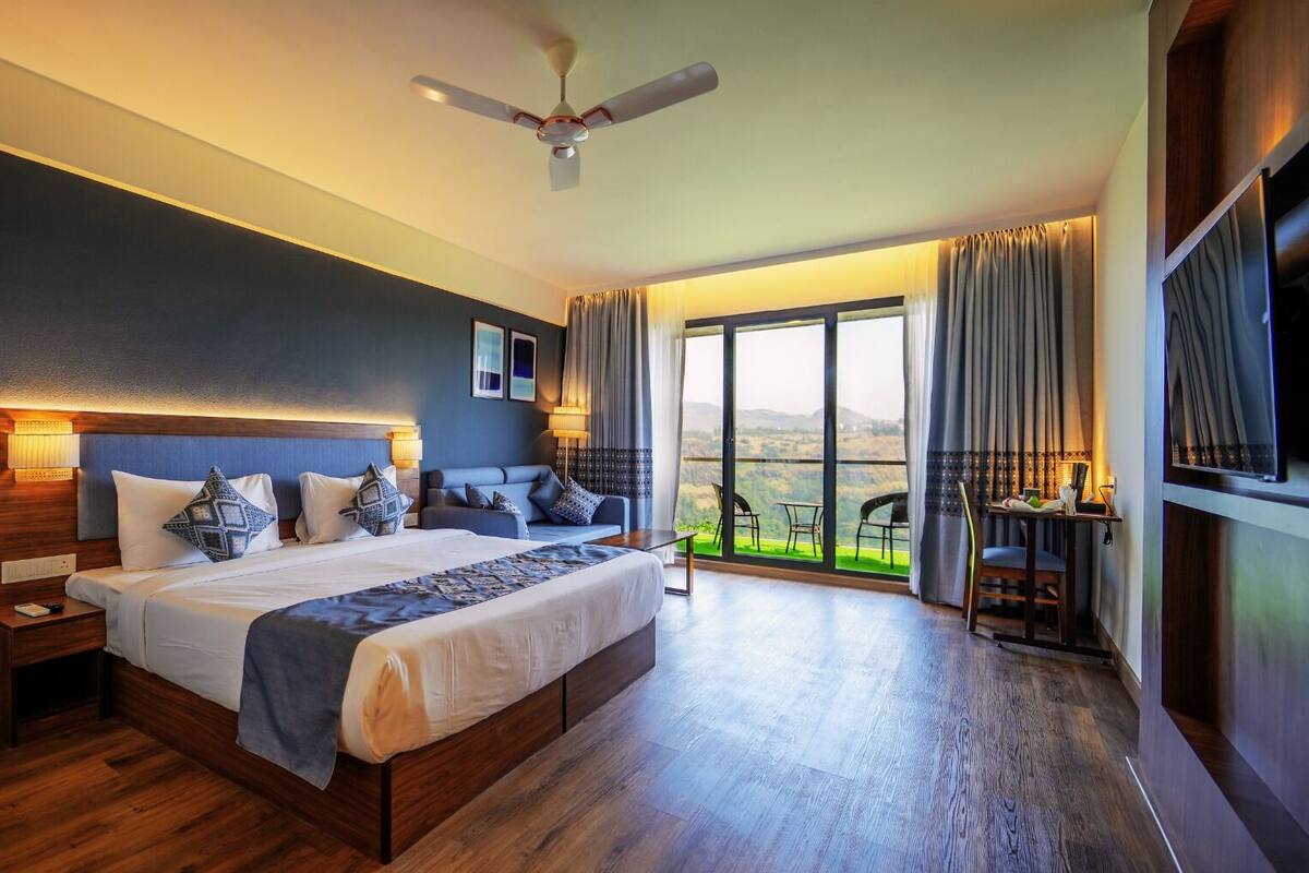A spacious bedroom with a large bed, a ceiling fan, and a view of the outdoors through large windows.