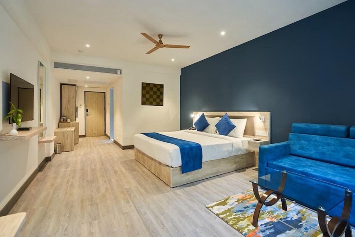 Una habitación de hotel moderna con una cama grande, un sofá azul y un ventilador de techo.