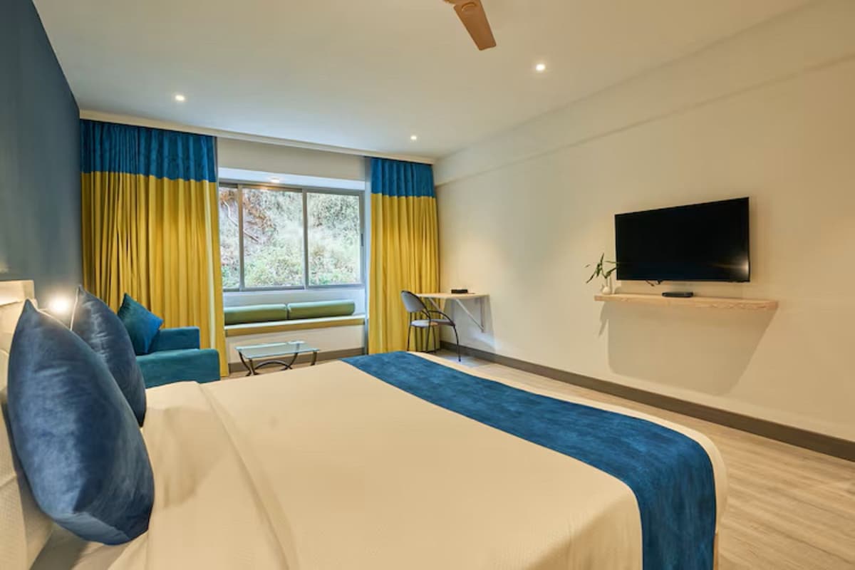 A hotel room with a large bed, a desk, a chair, a TV, and a window with curtains.