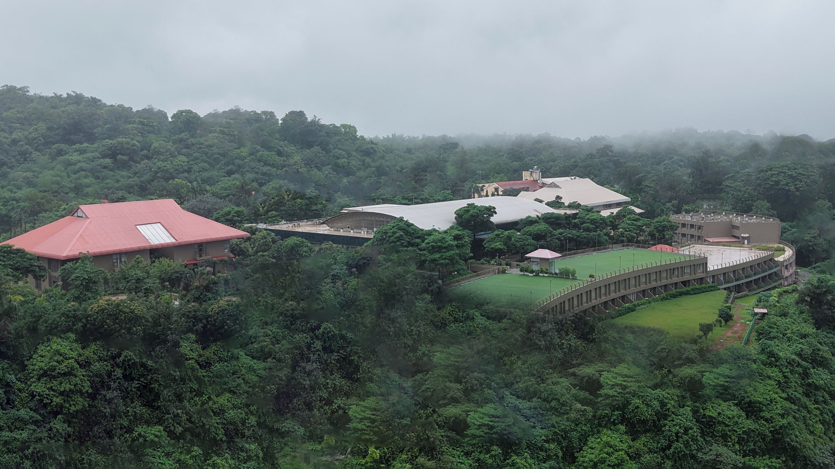 A large building with a red roof, surrounded by dense green forest.