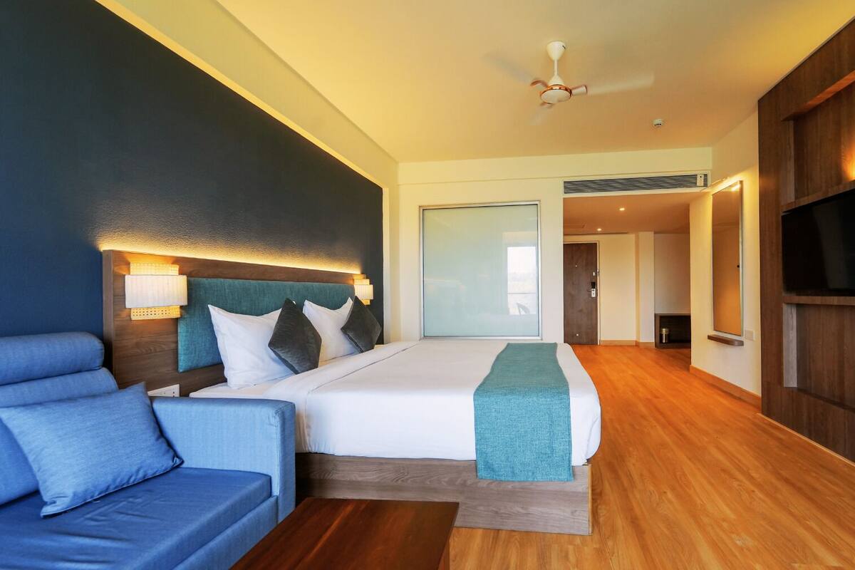 A modern hotel room with a large bed, a sofa, a TV, and a fireplace.