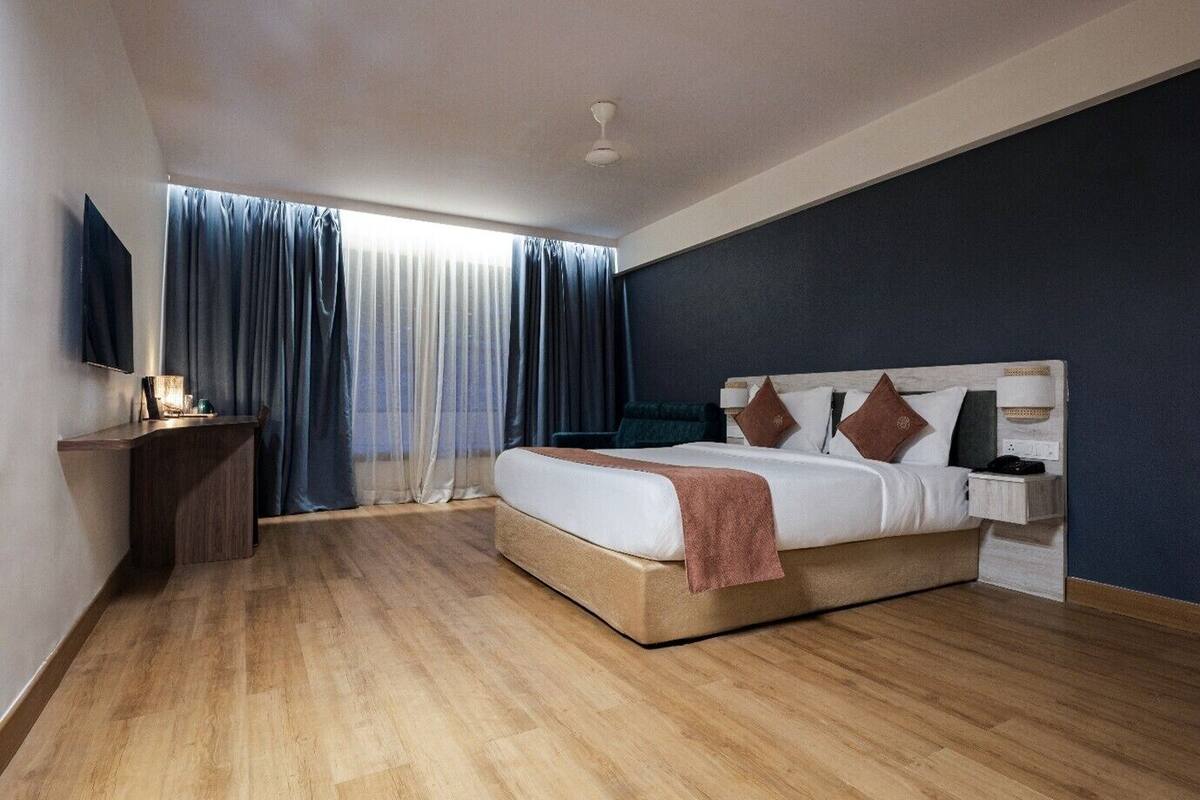 A modern hotel room with a large bed, a desk, a TV, and a view of the outdoors.