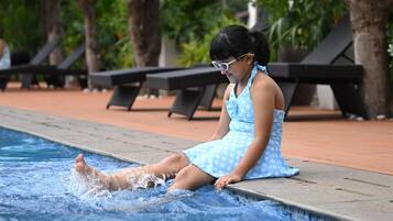A person sitting by a pool with lounge chairs and trees in the background.