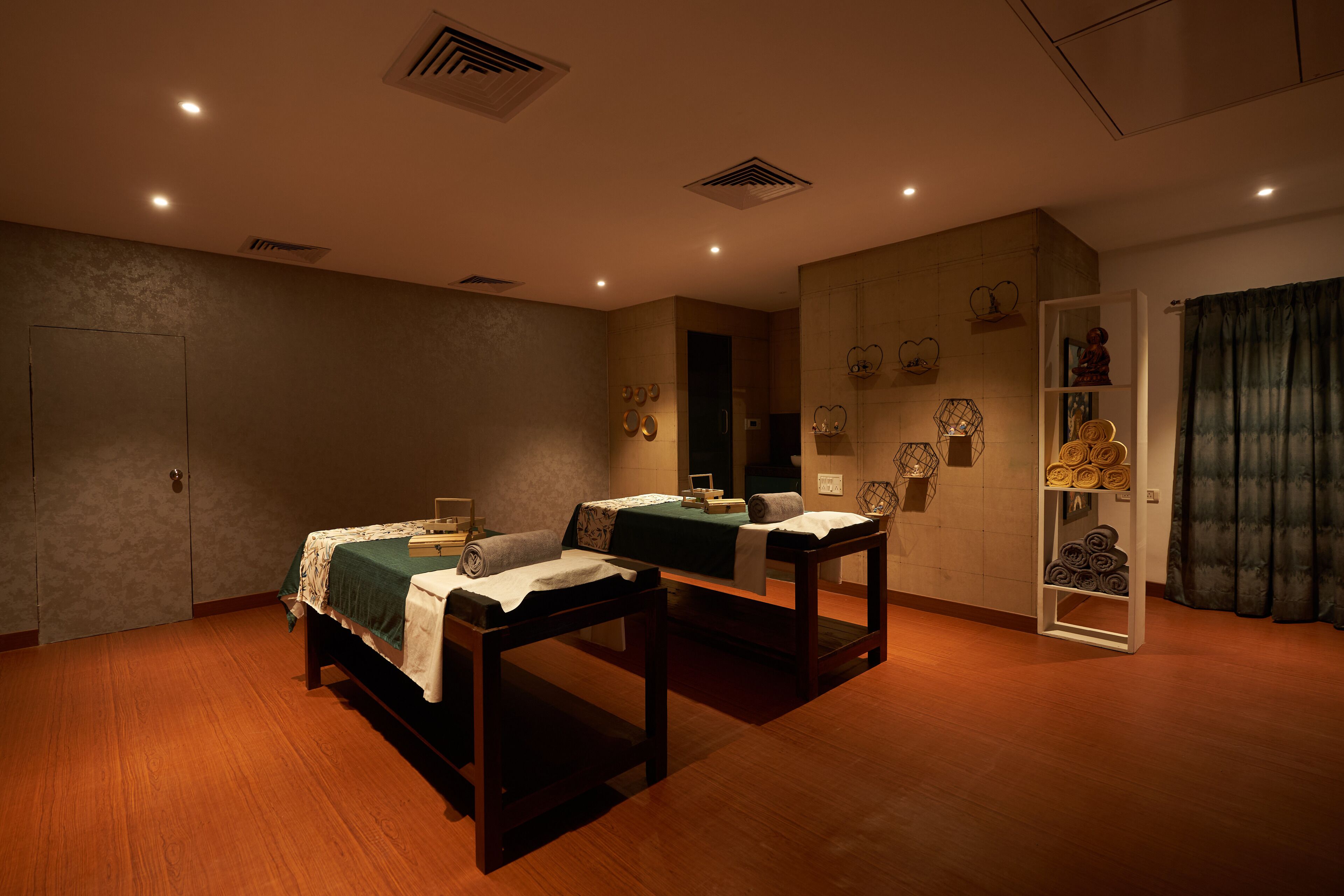 A room with two beds, a shelf with towels, and a cabinet with decorative items.