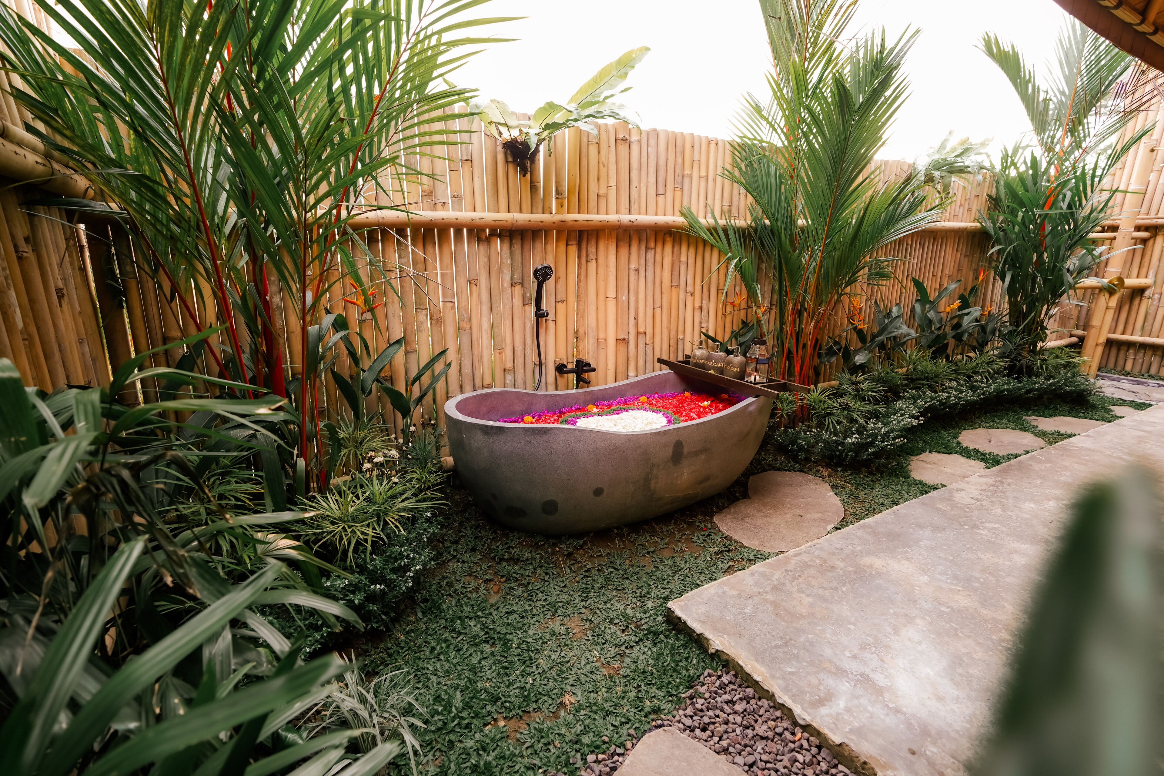A garden with a hot tub surrounded by lush greenery and a bamboo fence.