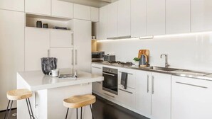 Eine moderne Küche mit weißen Schränken, einer zentralen Kochinsel mit Barhocker, einem eingebauten Backofen und einer Edelstahl-Spüle.