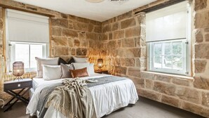 Ein Schlafzimmer mit Steingemäuer, einem Bett mit vielen Kissen, einem Nachttisch mit Lampe und einem Fenster mit Blick.