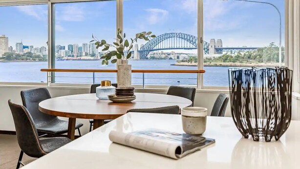 Ein Essbereich mit Blick auf die Sydney Harbour Bridge, einem runden Tisch, schwarzen Ledersesseln und einer dekorativen Vase.