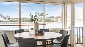 Ein Essbereich mit einem runden Tisch, sechs Stühlen, einer Vase mit Grünpflanzen und Blick auf eine Brücke und einen Fluss.