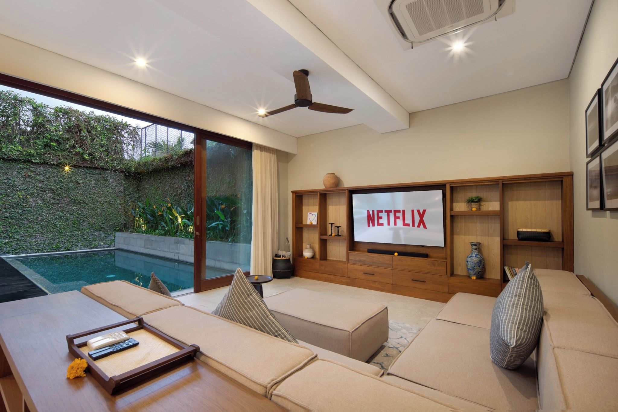 A modern living room with a large TV screen displaying 'NETFLIX,' a pool outside, and a ceiling fan.