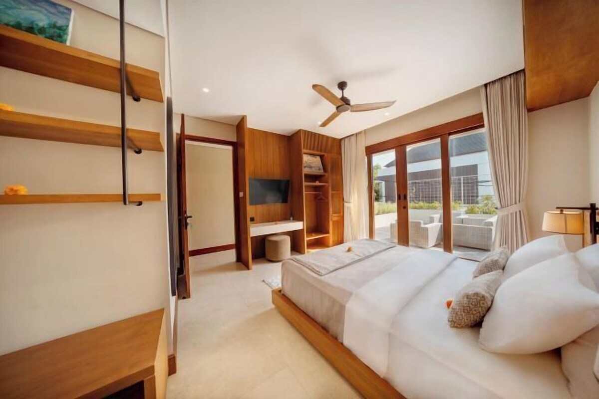 A bedroom with a bed, a ceiling fan, a TV, a wooden wardrobe, and a balcony with outdoor furniture.