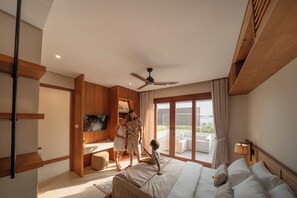 A modern hotel room with a bed, a TV, a ceiling fan, and a balcony with outdoor furniture. - Kolila Villa Seminyak by Ini Vie Hospitality (Kerobokan)