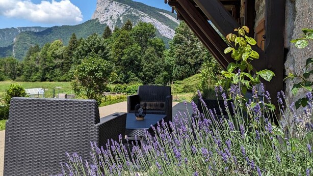 An outdoor seating area with wicker furniture, surrounded by lavender plants, and a mountain backdrop. - Gîte La P'tite Lulu à St Pierre D'entremont, à Côté Cirque de St Même (Saint-Pierre-d'Entremont)