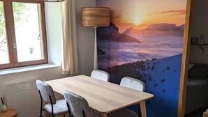 A dining area with a wooden table and four chairs, a lamp, and a mural of a mountainous landscape. - Gîte La P'tite Lulu à St Pierre D'entremont, à Côté Cirque de St Même (Saint-Pierre-d'Entremont)