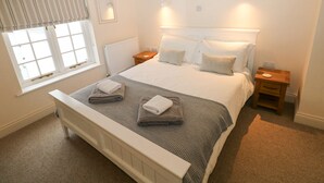 Un dormitorio ordenado con una cama grande, dos mesitas de noche, una ventana con cortinas y un radiador.