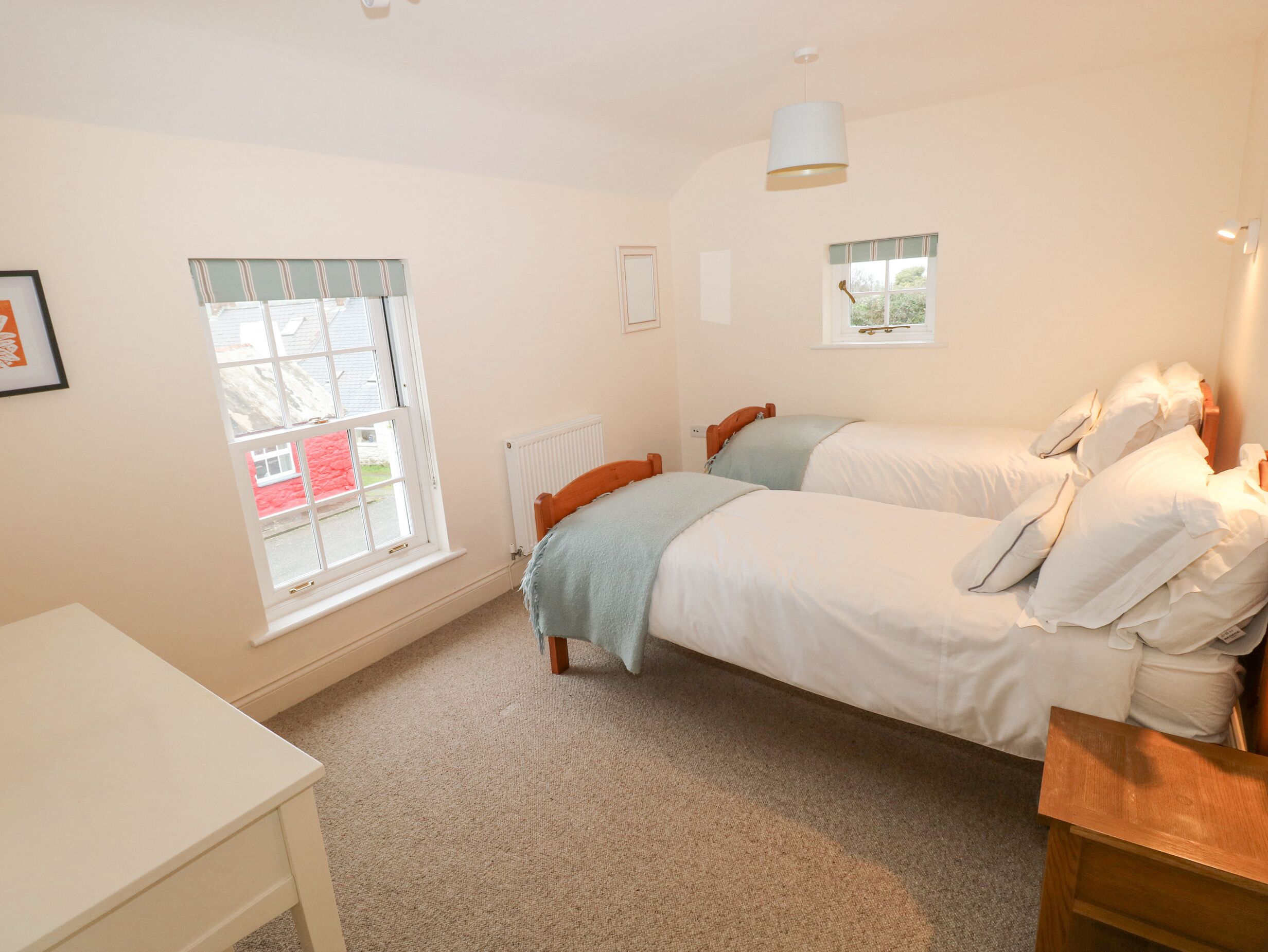 A bedroom with two beds, a window, a radiator, and a desk.